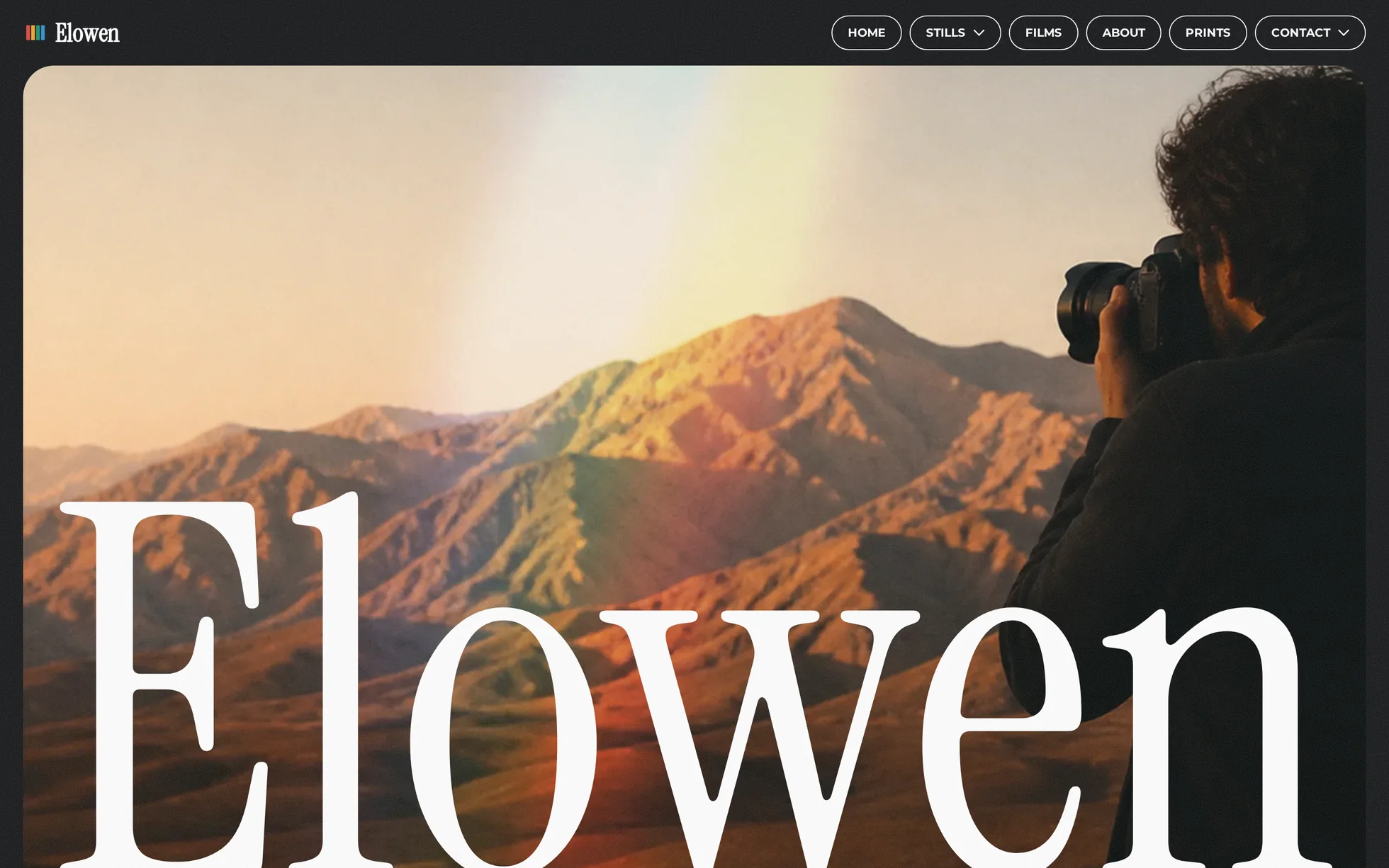 Preview of the Elowen template: a full-screen photograph of a photographer framing desert mountains at sunrise, crossed by a prism of light, with the wordmark “Elowen” bleeding off the bottom edge.