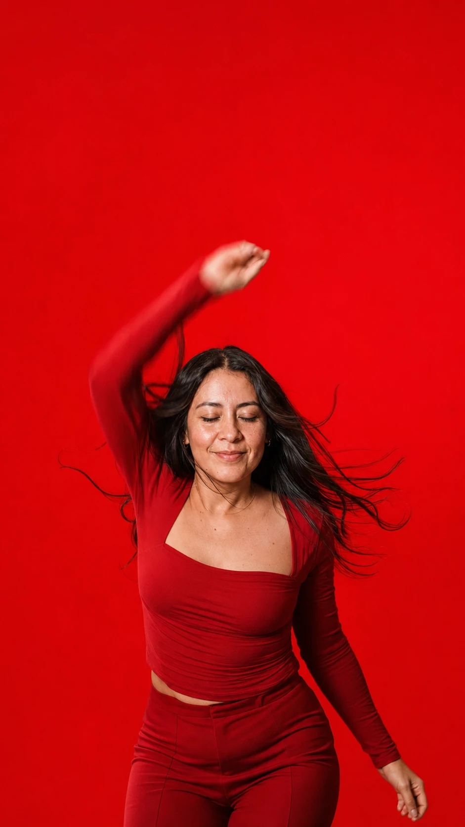Portrait on a bright red background: a woman in an open shirt, one arm raised above her head.