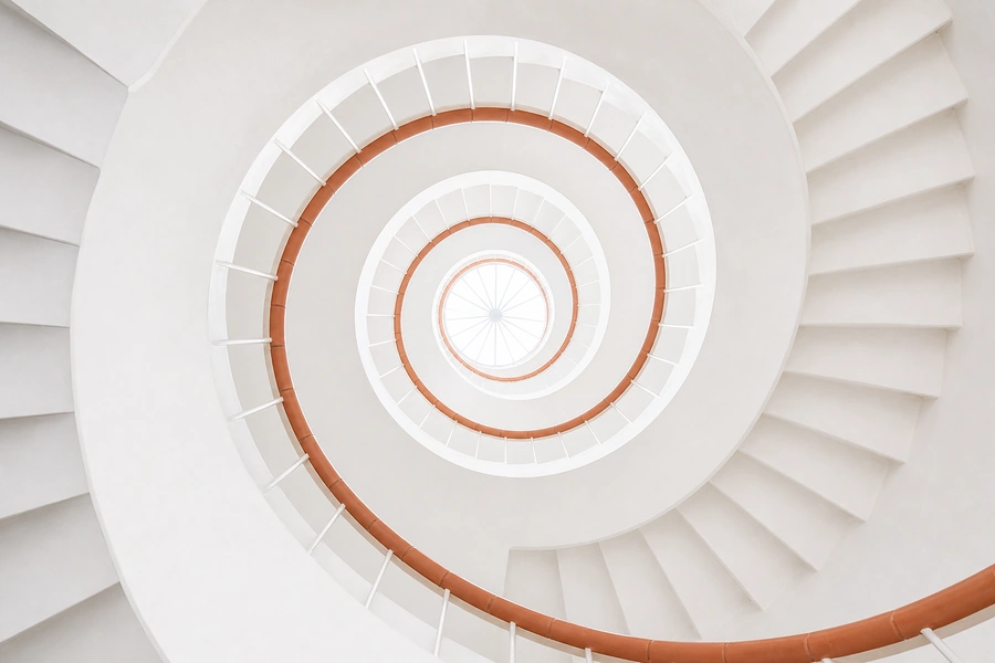 A white spiral staircase seen from below, up towards a round skylight