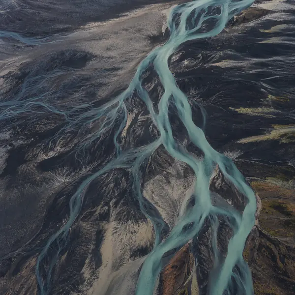 Aerial view of a turquoise glacial river branching through black volcanic sand.