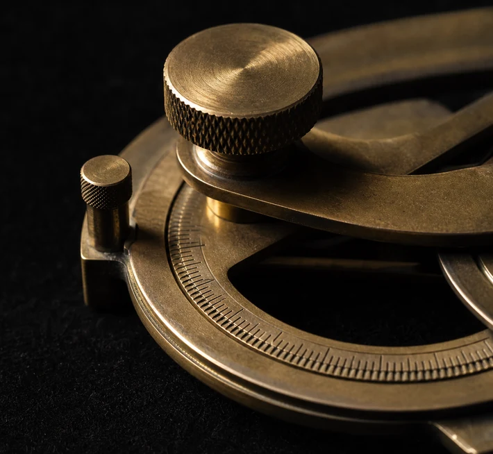 A brass measuring instrument in close-up: graduated limb and knurled wheel on a black background.