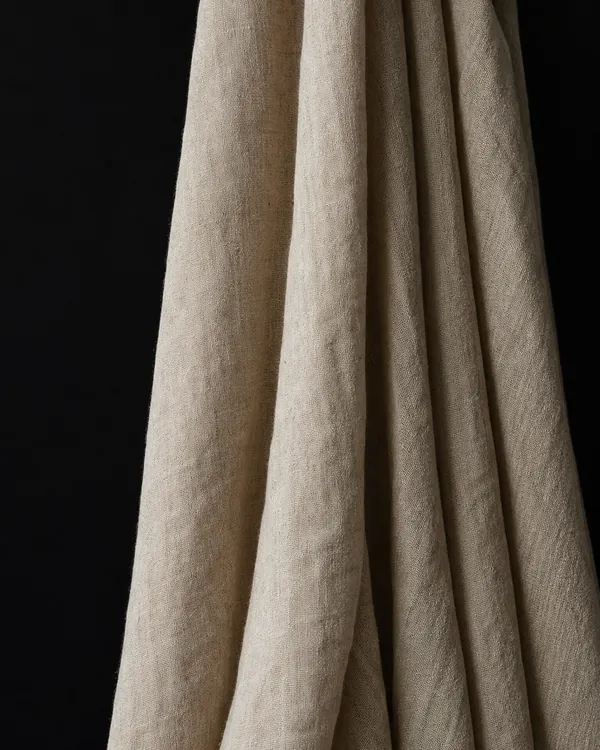 Unbleached linen cloth hanging in soft vertical folds, set against a black background.