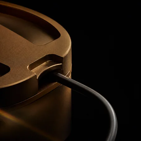 A detail of a deep amber machined object with a dark cable curving away