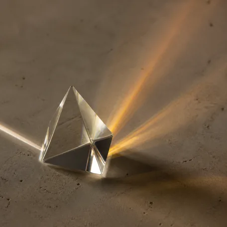 A faceted glass prism splitting a beam of light into an amber fan