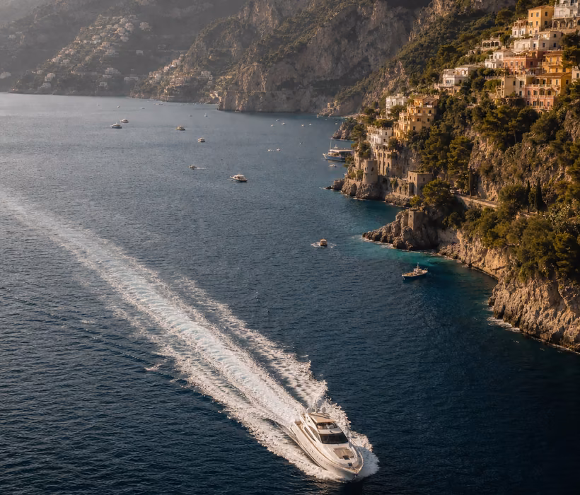 Luxury yacht sailing along the Amalfi Coast cliffs.