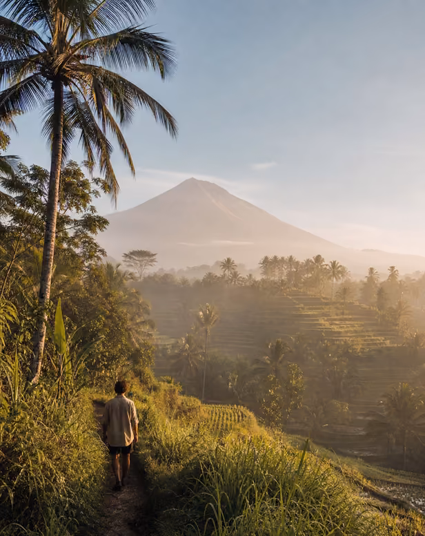 Hiker on jungle trail overlooking Bali volcano.