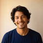 Smiling man with curly brown hair wearing a dark blue shirt.