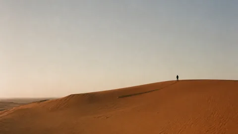 A lone walker on the crest of a sand dune.