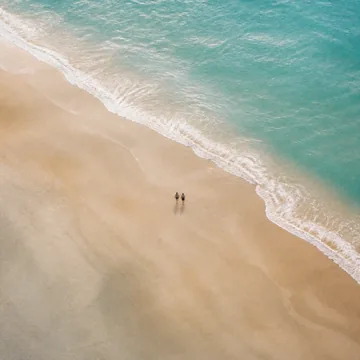 Two figures walking the tideline of an empty beach.