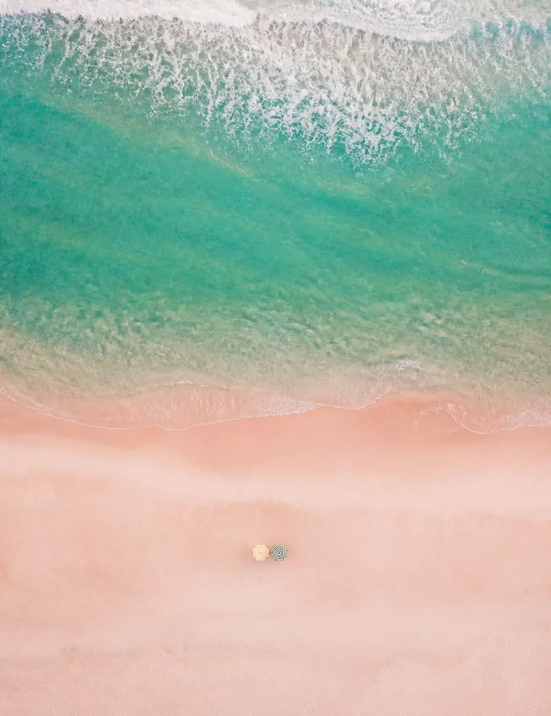 Turquoise surf breaking on pink sand, seen from above.