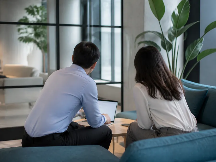 Two colleagues talking over a laptop in an office lounge