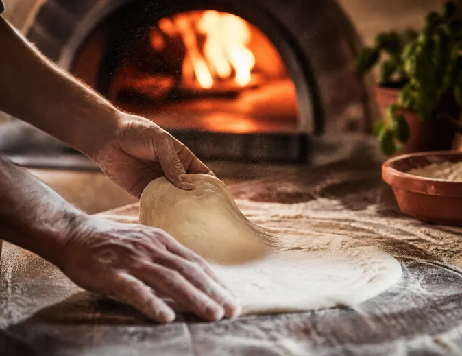 Pizza dough being stretched on a floured bench.