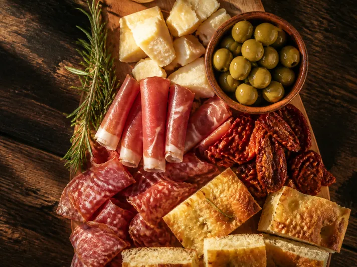 An antipasti board with cured meats, olives and focaccia.