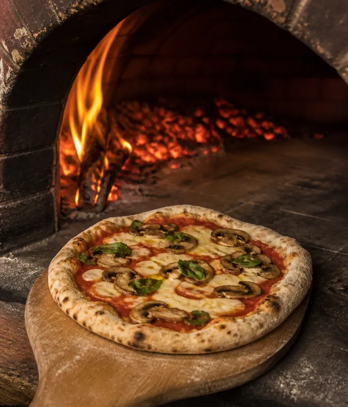 The mouth of the wood-fired oven with a pizza on the peel.