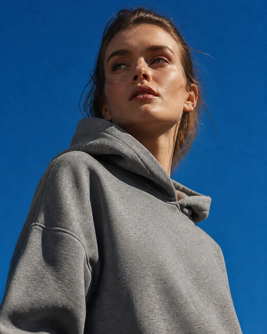 A woman in a grey hooded sweatshirt against an open sky