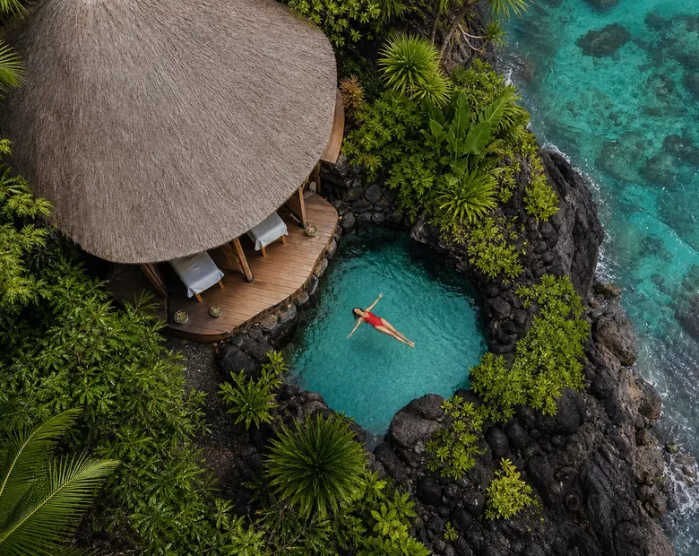 An open-air spa pavilion with a thatched roof beside a small turquoise pool in dark rock
