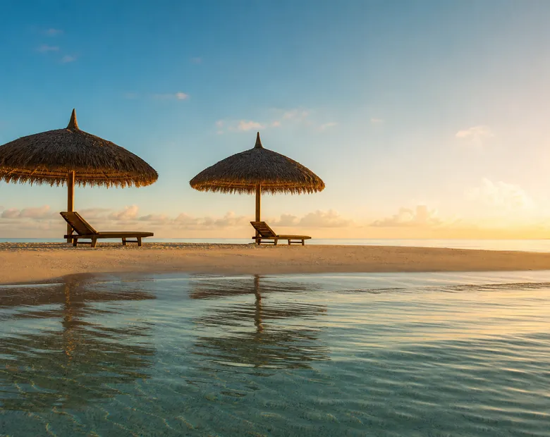 Two thatched parasols and wooden loungers on a deserted sandbank at golden hour