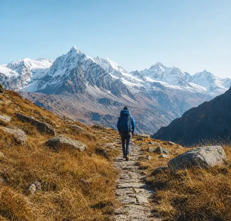 Hiker on a stone path below snow-capped peaks