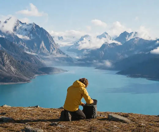 Traveller in a yellow jacket kneeling on a rocky plateau