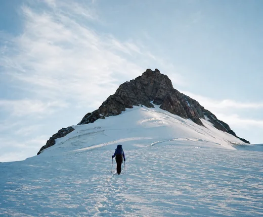 Hiker climbing a snow field below a summit