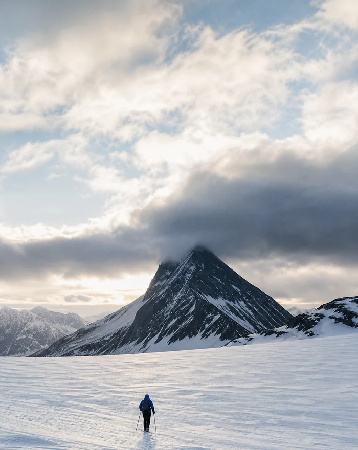 Trekker crossing a snow field towards a dark peak