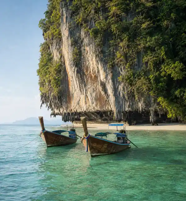 Longtail boats moored under a limestone cliff