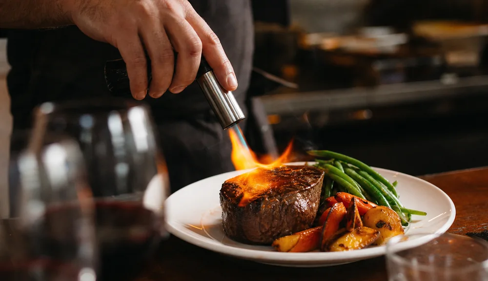 A chef finishing a beef fillet with a blowtorch