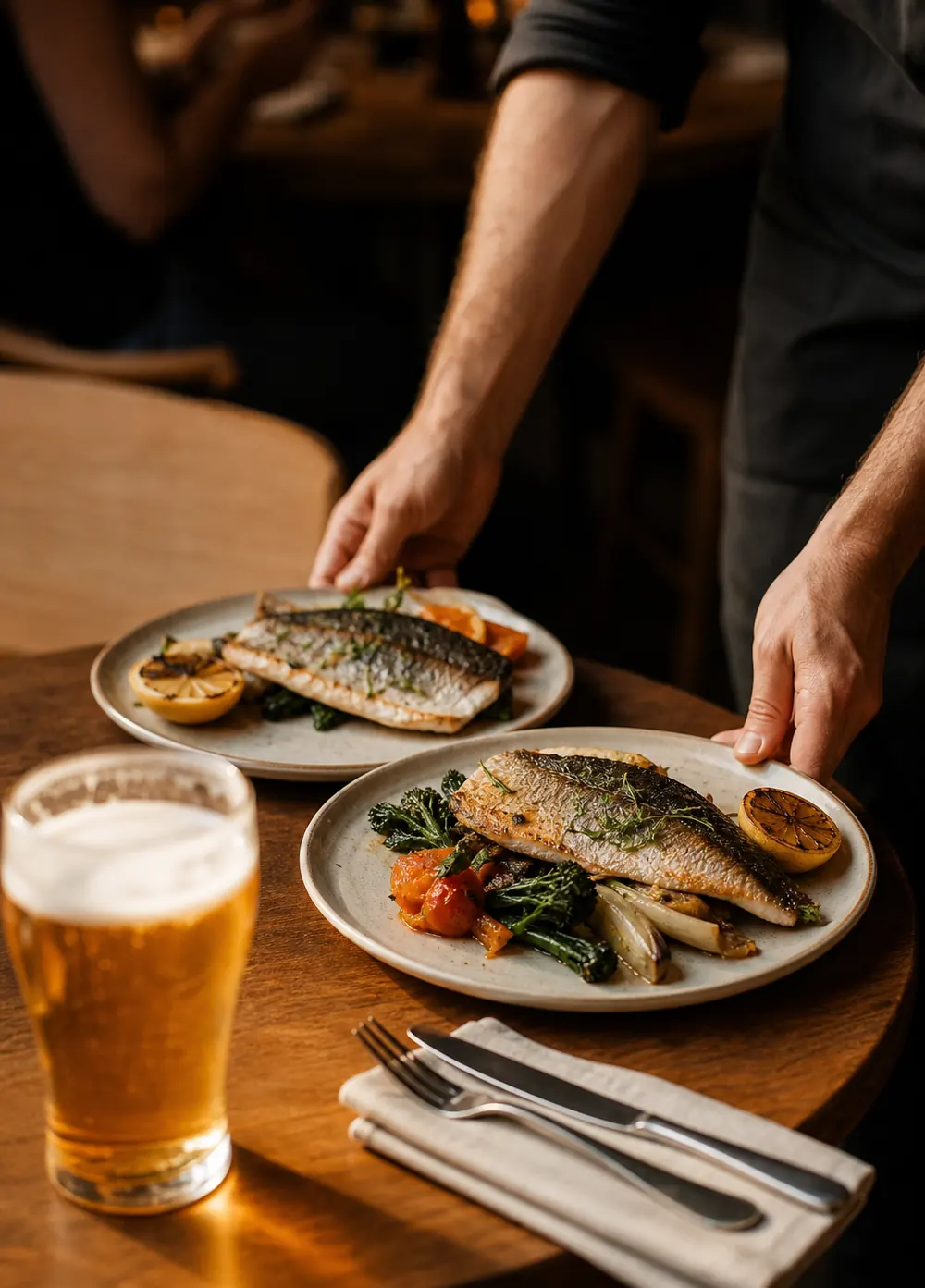 A waiter setting two plates down beside a beer