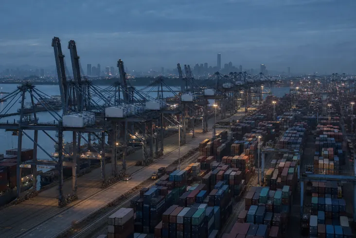Container terminal at dusk with gantry cranes over stacked containers.