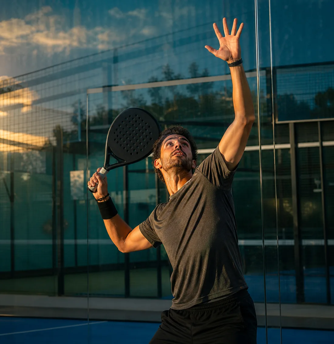 A player mid-serve seen through the glass wall of the court.